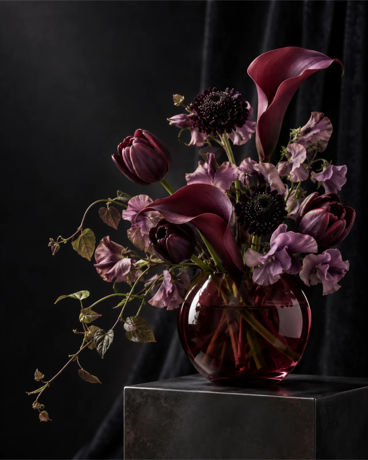 Plum calla lilies and mauve sweet peas in dark glass